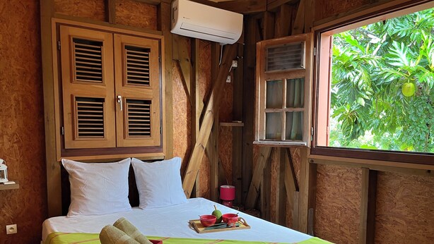 A wooden room with a bed, a window with a view of greenery, and an air conditioning unit. - Villa Familiale 8p Piscine Sécurisée & Jardin PMR (Le Gosier)