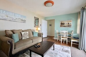 A living room with a sofa, coffee table, and dining area with chairs.