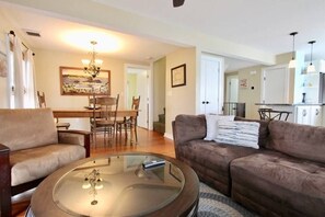 A living room with a brown sofa, a glass coffee table, and a dining area with wooden furniture.
