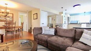 Ein Wohnzimmer mit einem braunen Sofa, einem Glastisch und einem Essbereich mit Holzsesseln und einem Tisch.