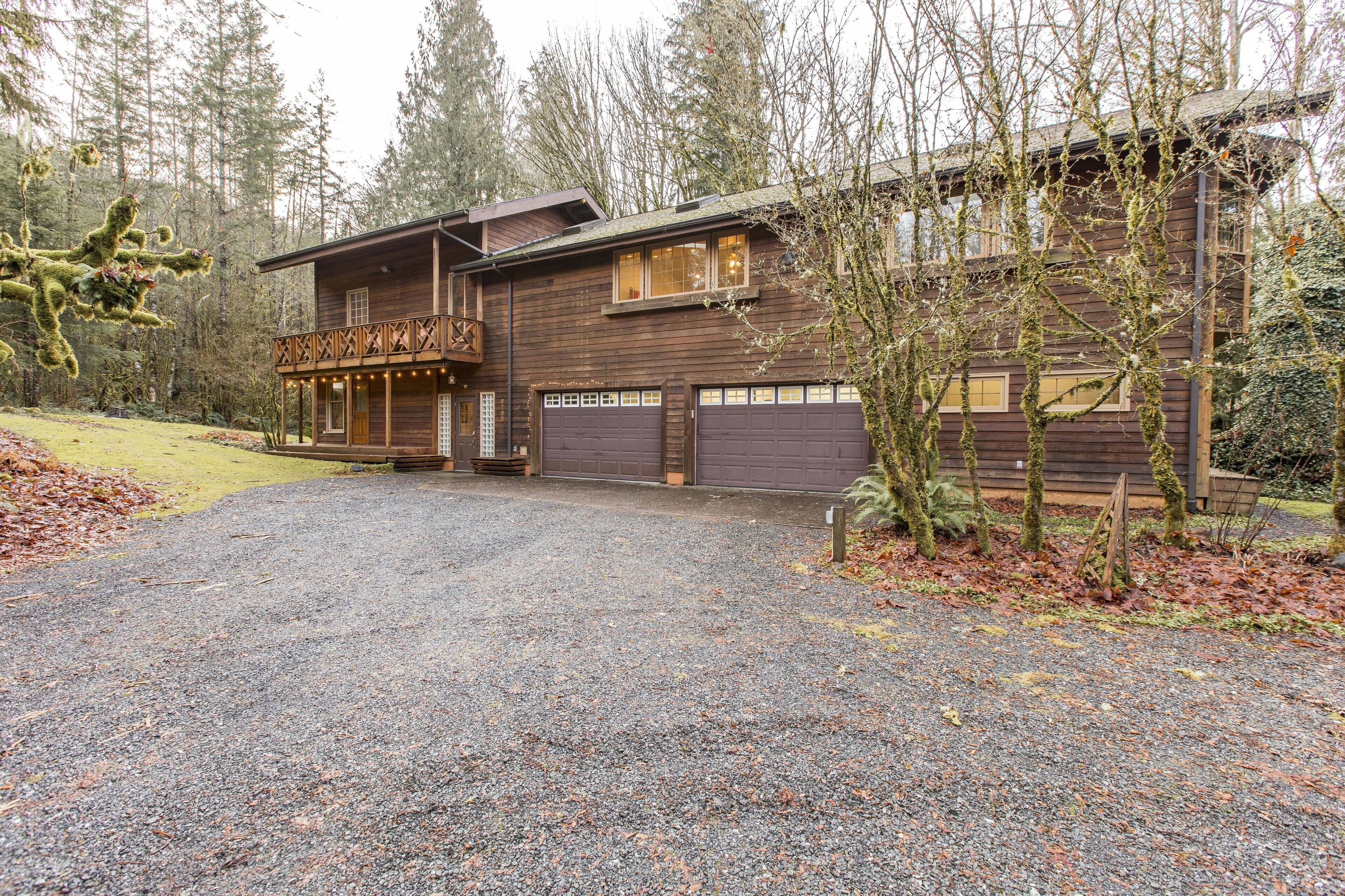 A rustic wooden house with a covered porch and a gravel driveway.