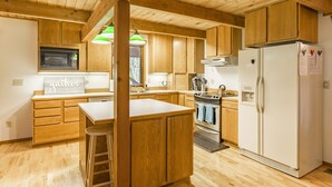 A kitchen with wooden cabinets, a central island with a stool, a refrigerator, and a stove. - 4,000 sqft Mt. Baker Ski Lodge, sleeps 21, walk to town, hot tub, fiber internet (Glacier)