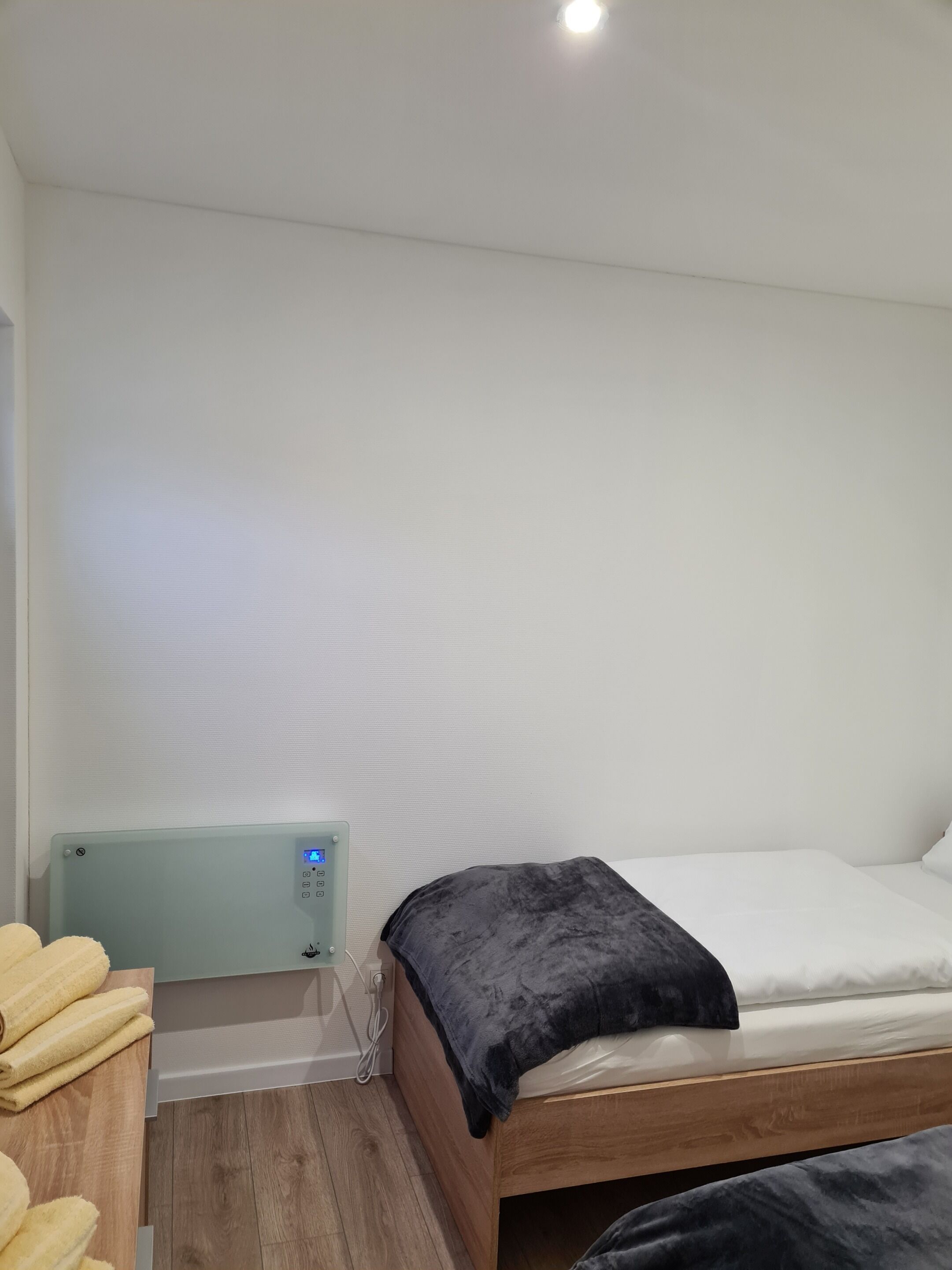 Ein kleiner, ordentlicher Raum mit einem Bett, einem Nachttisch mit Handtüchern und einem an der Wand montierten Heizkörper.