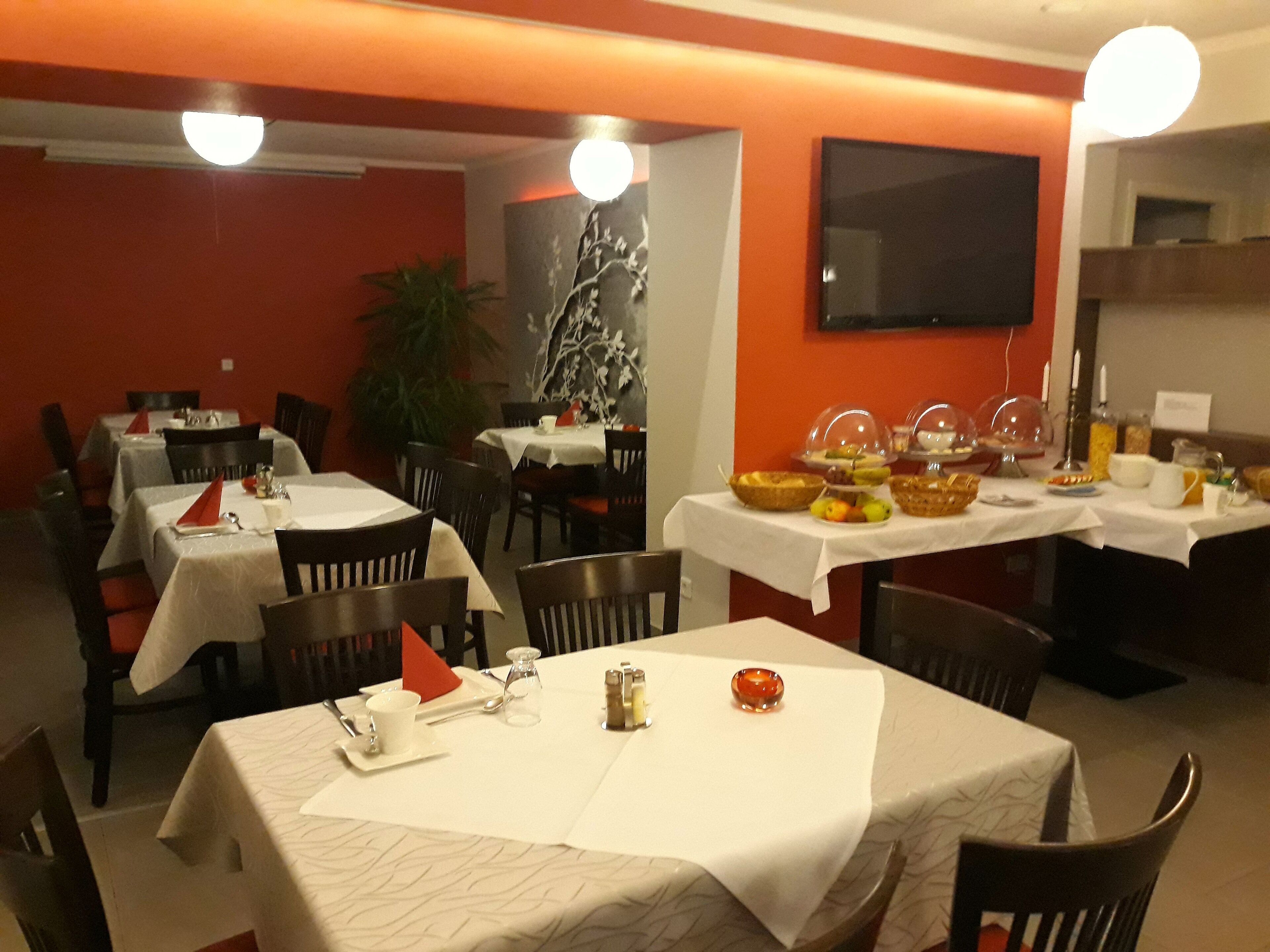 Un restaurante con varias mesas, algunas con manteles blancos y otras sin ellas. Hay sillas alrededor de las mesas, y se ve una planta al fondo.