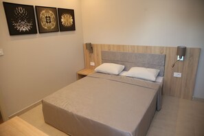 A neatly made bed with a grey bedspread and two pillows, a wooden headboard, a nightstand with a lamp, and three wall art pieces above the bed.