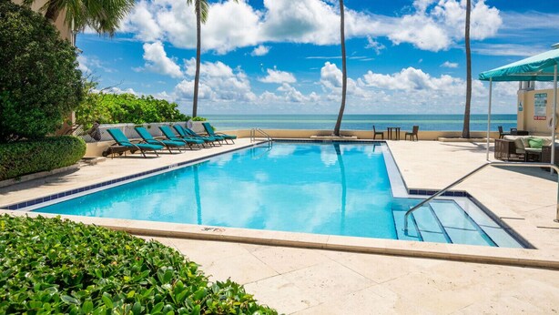 A swimming pool with lounge chairs and palm trees, overlooking a beach. - Exclusive Key West Beach Front - 2BR Luxury Condo w/Gym and Pool Access (Newly Refurnished!) (Key West)