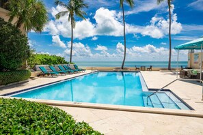 A swimming pool with lounge chairs and palm trees, overlooking a beach. - Exclusive Key West Beach Front - 2BR Luxury Condo w/Gym and Pool Access (Newly Refurnished!) (Key West)
