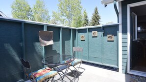 A patio with a glass table and chairs, a wooden bench, and a teal-painted wall with decorative cutouts.