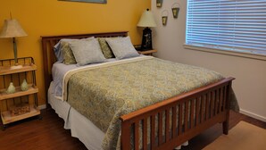 A bedroom with a wooden bed, a nightstand, a lamp, and a window with blinds.