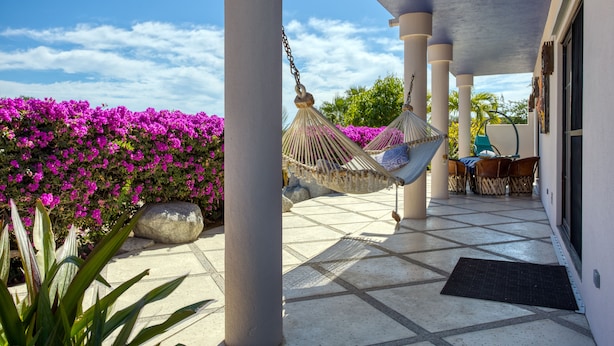 A covered patio with a hammock, a stone bench, and a view of purple flowers. - Sweeping ocean views steps to beach w/pool & Firepit. Close to Tres Palapas!  (Los Barriles)