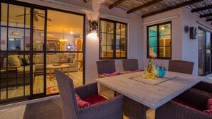 A dining area with wicker chairs and a wooden table, large windows, and a ceiling fan. - Sweeping ocean views steps to beach w/pool & Firepit. Close to Tres Palapas!  (Los Barriles)