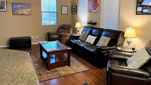 A living room with a leather sofa, a glass coffee table, a wooden side table, a black ottoman, and a ceiling fan. - Beautiful 3bd/3ba Phoenix Home near Downtown Area, ASU! (Phoenix)