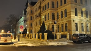 Un edificio histórico con arquitectura clásica, una calle cubierta de nieve y automóviles estacionados.