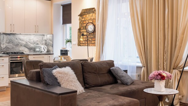 Una sala moderna con un sofá seccional marrón, una mesita blanca y un reloj de pared decorativo.