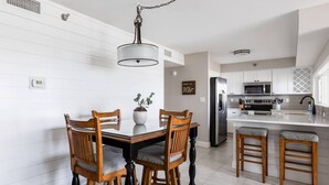 A modern kitchen with white cabinetry, a stainless steel refrigerator, and a central island with stools. - Newly remodeled high-end beach front condo. Gulf view from every room on 8 acres (Destin)