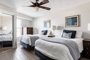 A hotel room with two beds, a ceiling fan, a dresser, and two framed artworks on the wall.