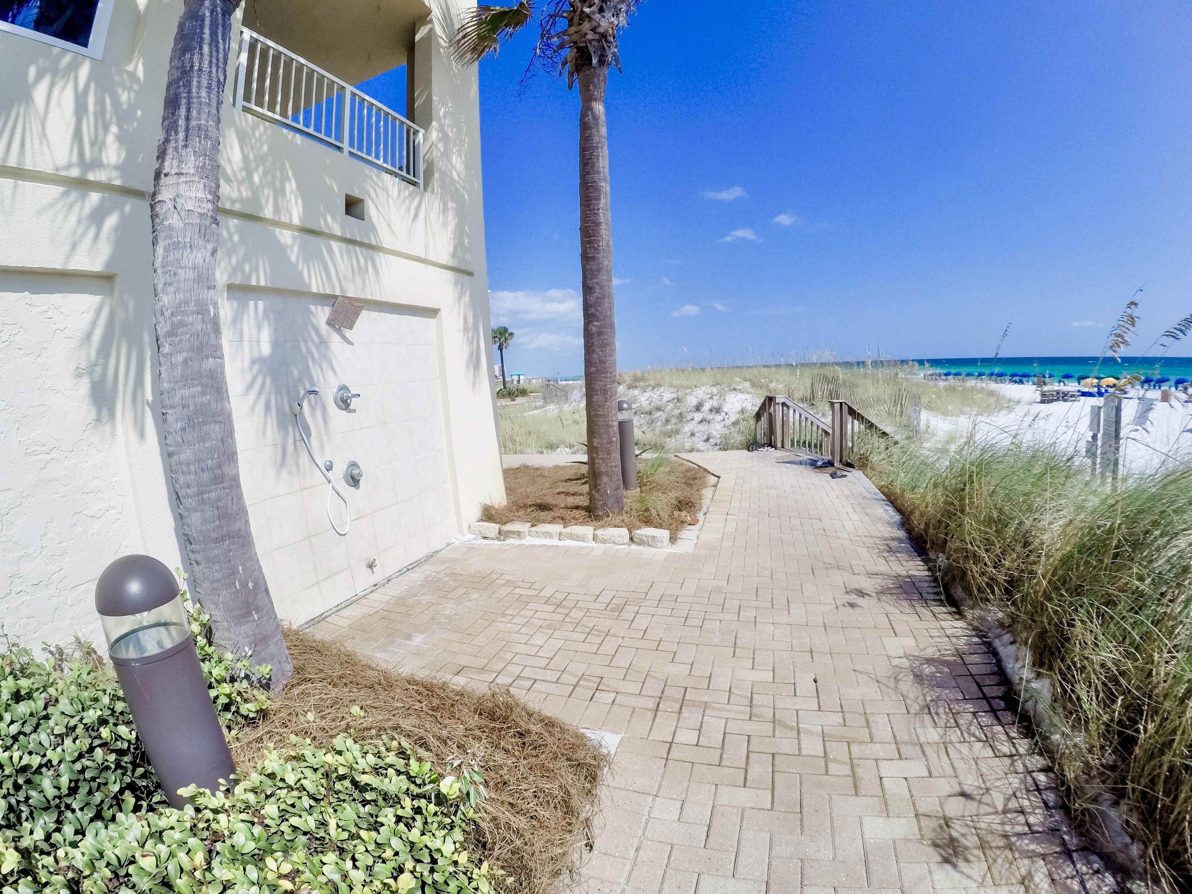 Un chemin menant à un bâtiment doté d’un balcon, d’un palmier et offrant une vue sur la plage.