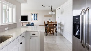 A modern kitchen with white cabinetry, a stainless steel refrigerator, and a dining area with a table and chairs. - Newly remodeled high-end beach front condo. Gulf view from every room on 8 acres (Destin)