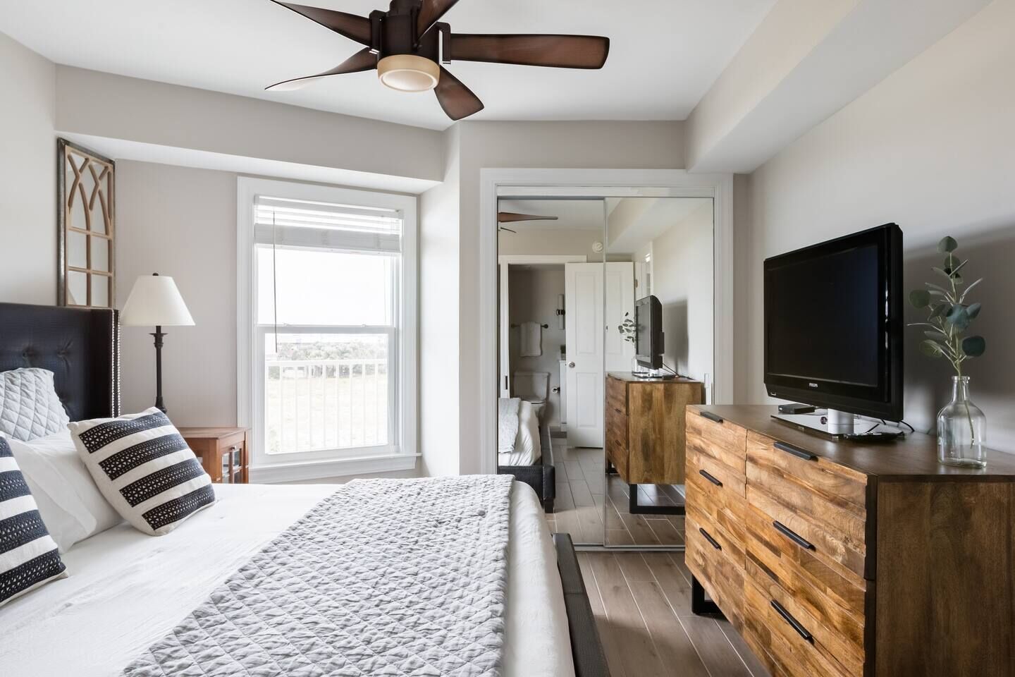 Une chambre à coucher avec un lit, une télévision, une commode et un ventilateur de plafond.
