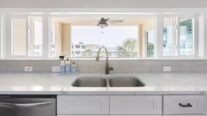 A kitchen with a large window, a ceiling fan, and a view of buildings and palm trees. - Newly remodeled high-end beach front condo. Gulf view from every room on 8 acres (Destin)