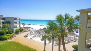 A beach view with a pathway leading to the beach, palm trees, and a building with a balcony.