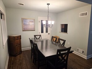 Comedor con una mesa rectangular, seis sillas, una araña, una puerta y un ventanal pequeño.