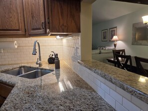 A kitchen with granite countertops, a double sink, wooden cabinets, and a tiled backsplash.