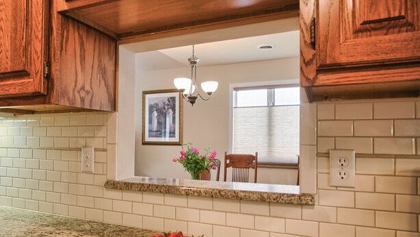 A kitchen with wooden cabinets, a granite countertop, a bowl of strawberries, a vase with flowers, and a framed picture on the wall. - Home in Mechanicsburg, PA close to  Carlisle, Camp Hill, Enola, Harrisburg area (Mechanicsburg)