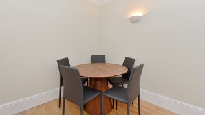 A round wooden table with six chairs, a white wall, and a wall-mounted light fixture.