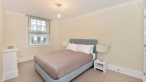A bedroom with a bed, a nightstand, a lamp, a window, and a ceiling light.