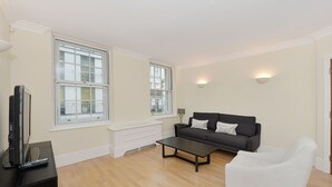 A living room with a dark sofa, a white armchair, a coffee table, and a TV on a stand.