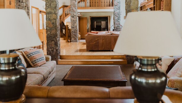 A spacious living area with a high ceiling, stone pillars, a wooden staircase, and a cozy seating arrangement. - The Ultimate Lodge for retreats, family reunions or Destination Weddings (Atlanta)