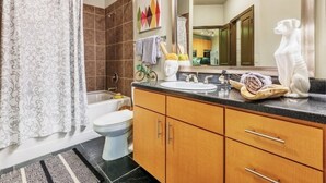 A bathroom with a bathtub, toilet, sink, and wooden cabinets. - Oakwood at Mosaic South End (Charlotte)