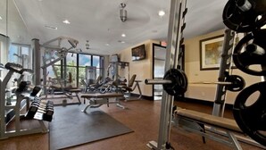 A gym with various exercise equipment, a large mirror, and a window providing a view of the outdoors. - Oakwood at Mosaic South End (Charlotte)