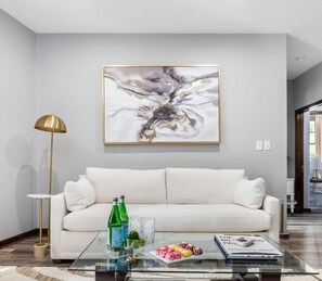 Una sala de estar moderna con un sofá blanco, una mesa de centro de vidrio y un cuadro abstracto grande en la pared.