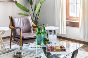 A glass-top table with bottles, glasses, and pastries in a well-lit room with a leather chair and a plant in the background. - Walk Everywhere! Near Marion Square & King Street's Best Restaurants + Shops (Charleston)