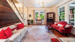 A spacious living room with a large staircase, a red sofa, a white sofa, and a chandelier.