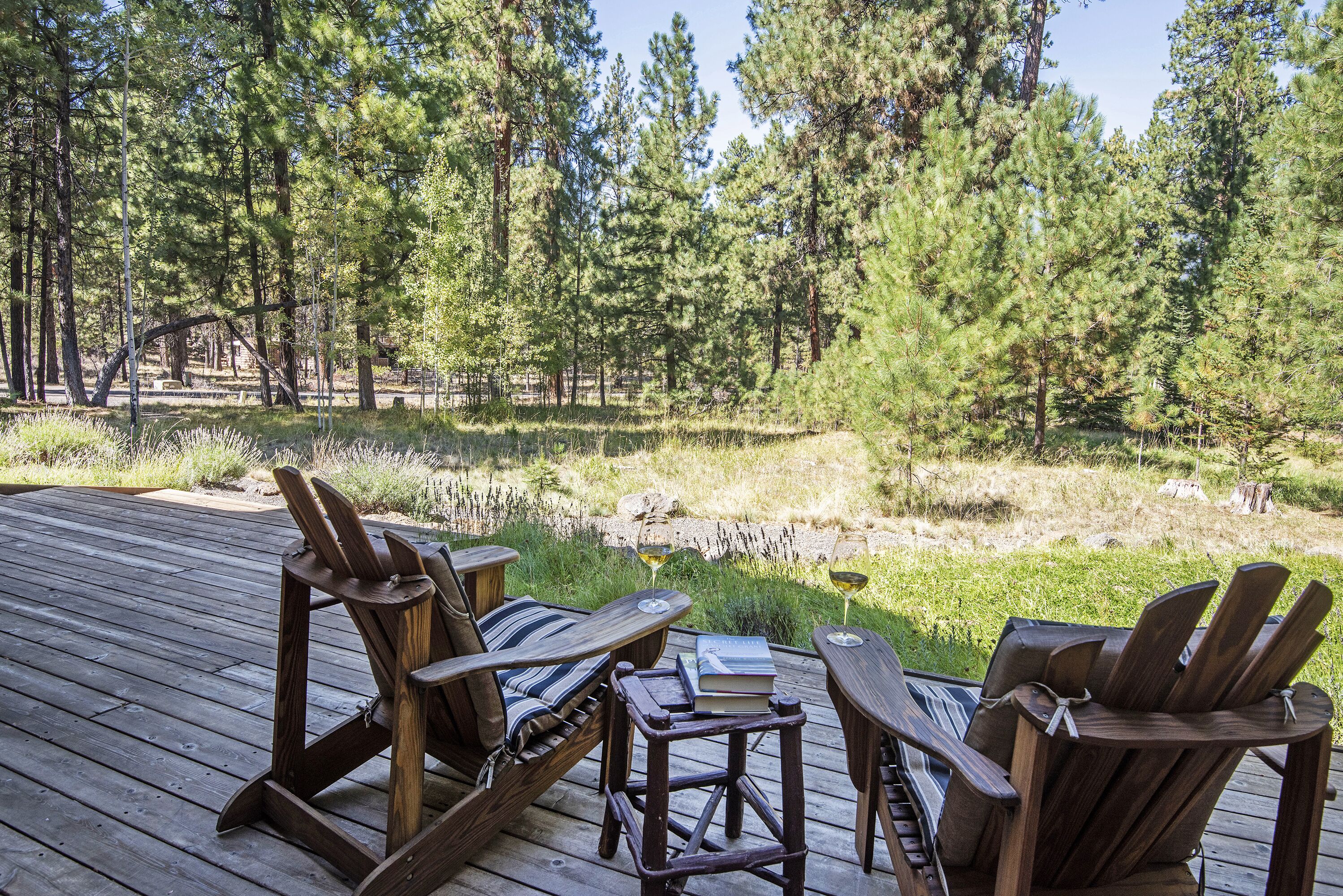 A wooden deck with Adirondack chairs and a small table, overlooking a forested area.