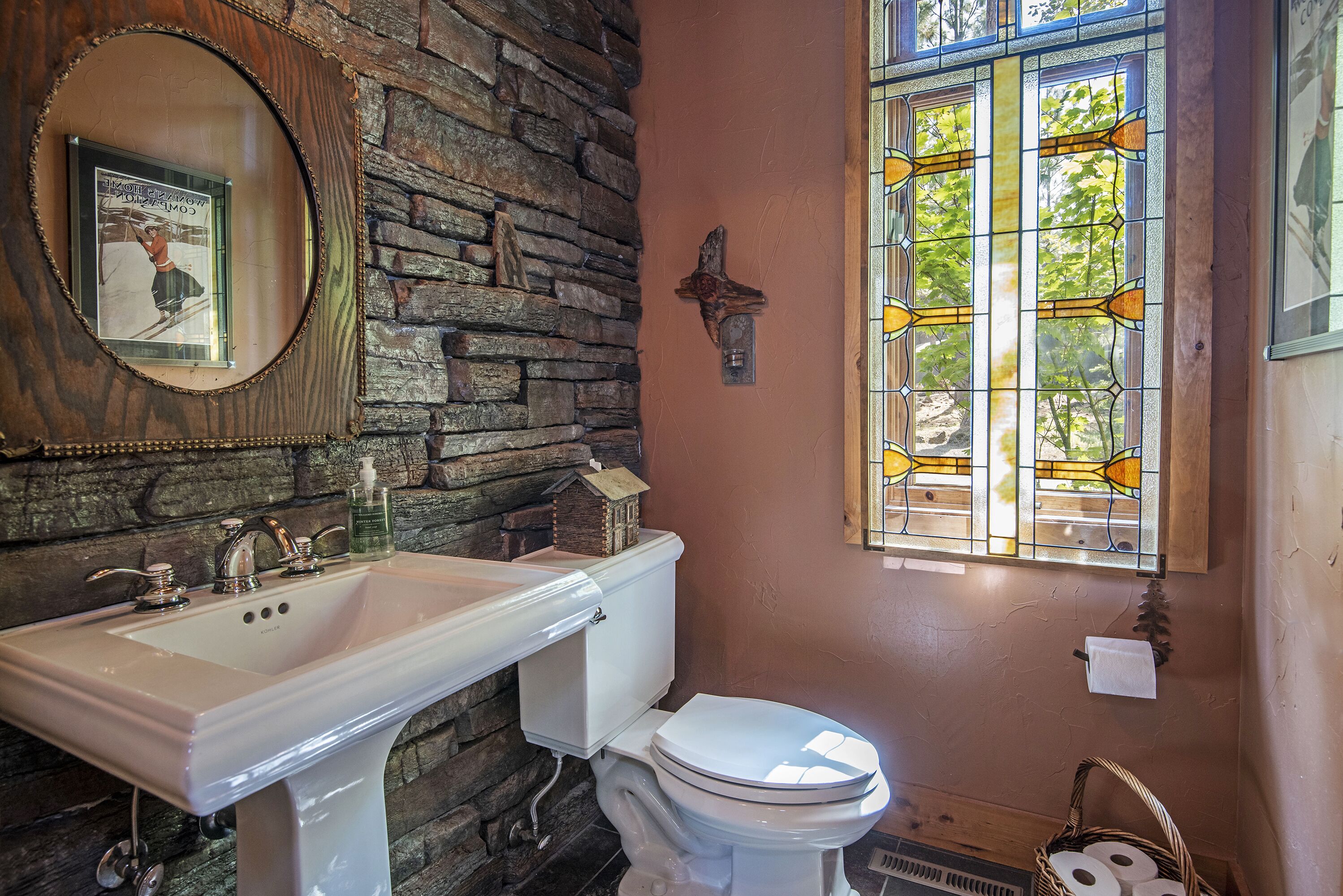 A bathroom with a stone wall, a white sink, a white toilet, and a stained glass window.