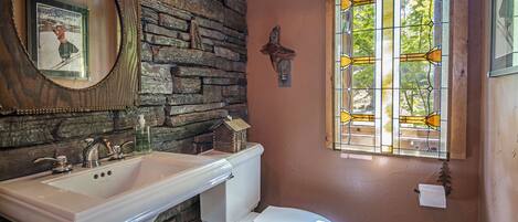 A bathroom with a stone wall, a white sink, a white toilet, and a stained glass window.