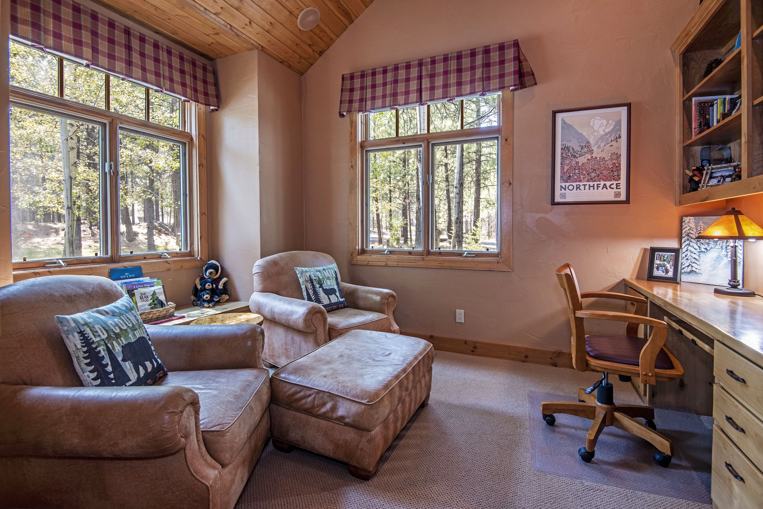 A cozy room with a large window, a wooden desk, a comfortable chair, and a bookshelf.