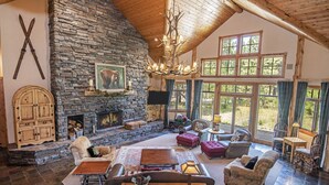 A cozy lodge interior with a stone fireplace, wooden furniture, and large windows. - LUXURY RUSTIC LODGE IN BLACK BUTTE RANCH (Black Butte Ranch)