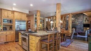 A spacious kitchen with wooden cabinets, a large island, and a stone fireplace. - LUXURY RUSTIC LODGE IN BLACK BUTTE RANCH (Black Butte Ranch)