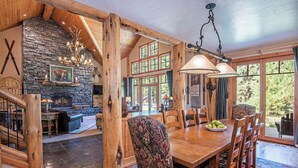 A rustic interior with a stone fireplace, wooden dining table, and large windows offering a view of the outdoors. - LUXURY RUSTIC LODGE IN BLACK BUTTE RANCH (Black Butte Ranch)