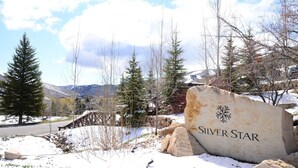 A large stone sign with the text "Silver Star" surrounded by snow, trees, and a wooden bridge.