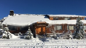 Eine Holzhütte mit dem Schriftzug 'Hostel', deren Dach mit Schnee bedeckt ist und von Eiszapfen verziert wird.