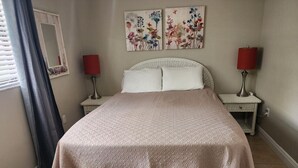 Un lit bien fait, recouvert d’une couverture à motifs, deux tables de chevet avec des lampes et une œuvre d’art florale accrochée au mur.