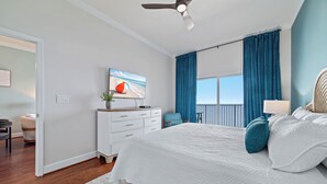 Un dormitorio con cama, televisor, cómoda, silla y vistas al exterior.