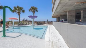 Piscina con palmeras, sillas de descanso y una zona cubierta.