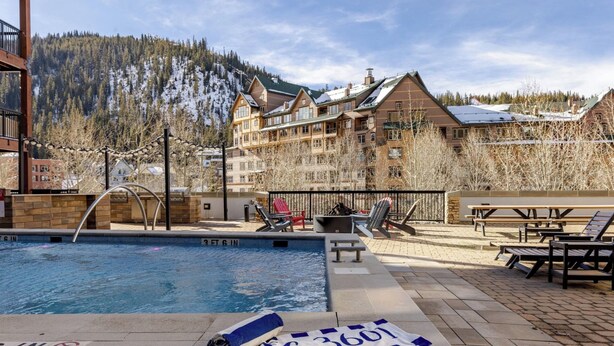 A pool area with lounge chairs and a towel rack, surrounded by a building with a view of a snowy mountain. - Newly Remodeled Studio steps from the lifts of Winter Park Base (Winter Park)